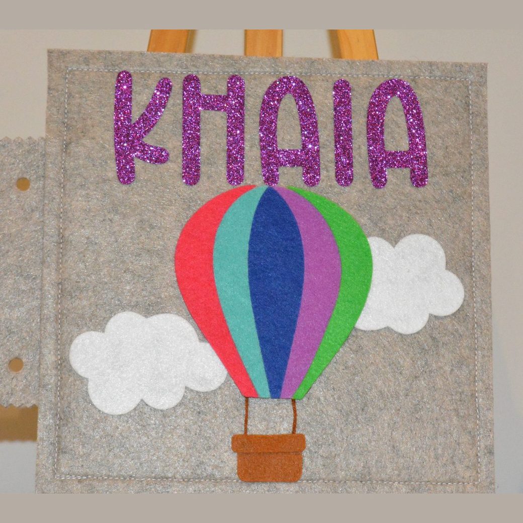 Felt busy book cover: a hot air balloon drifting between clouds, with a name above it in glitter