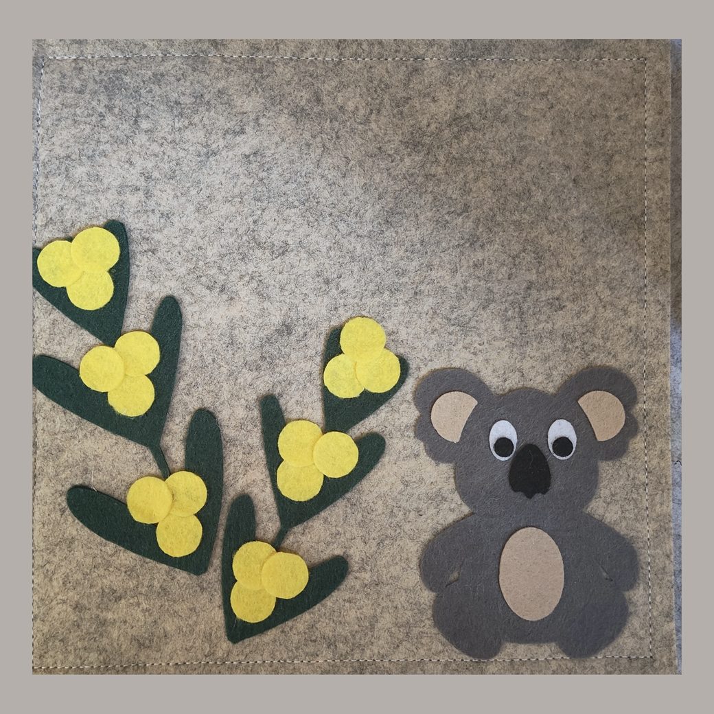 Felt busy book cover: a koala sitting under a spray of yellow wattle, on grey felt