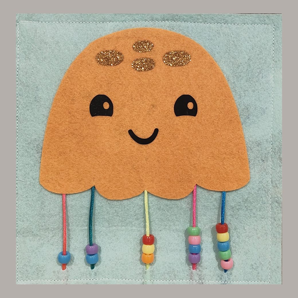 Felt busy book page: a smiling pink jellyfish with five strings of wooden beads for tentacles, on blue felt, orange