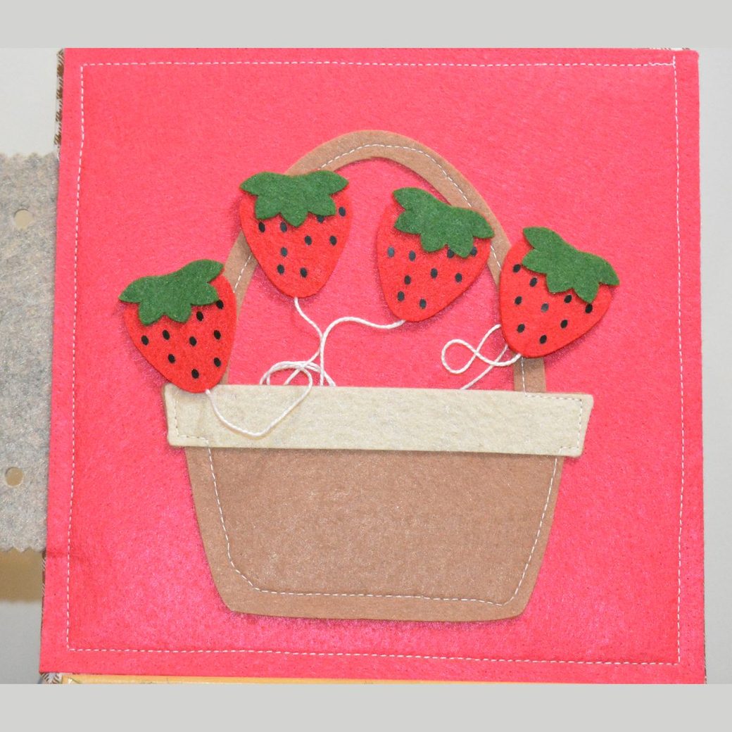 Felt busy book page: four red felt strawberries on a plant above a stitched basket with a pocket to drop them into, on strings